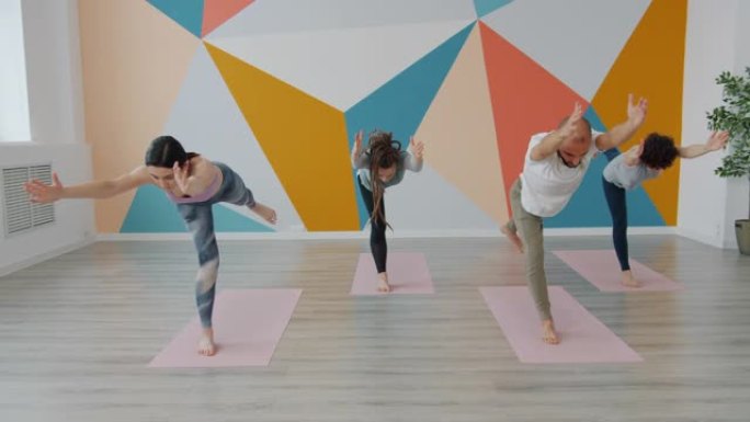 在瑜伽馆锻炼的年轻人的慢动作在垫子上做平衡体式