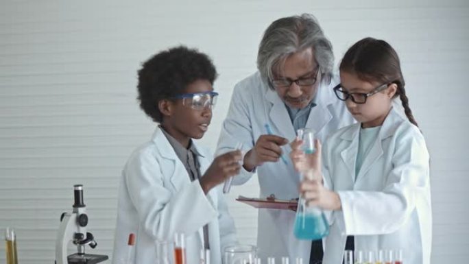 可爱的小男孩和女孩与高级老师进行科学实验