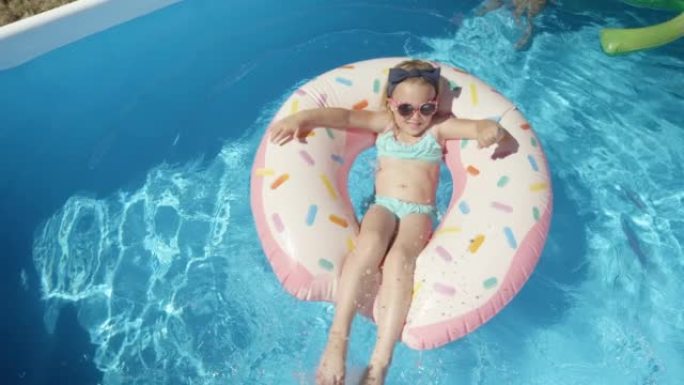 自上而下: 可爱的女孩，戴着墨镜在蓝色游泳池的浮动甜甜圈上