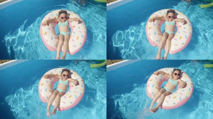 自上而下: 可爱的女孩，戴着墨镜在蓝色游泳池的浮动甜甜圈上