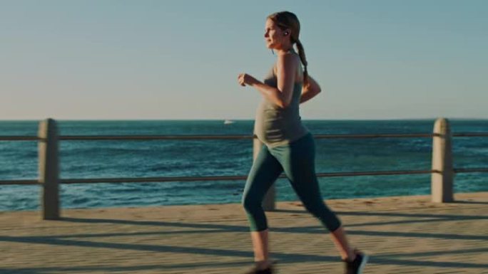 与女运动员一起在海边或海边的长廊上跑步，怀孕和健身。健康，健康和怀孕，女跑步者在户外训练时听音乐