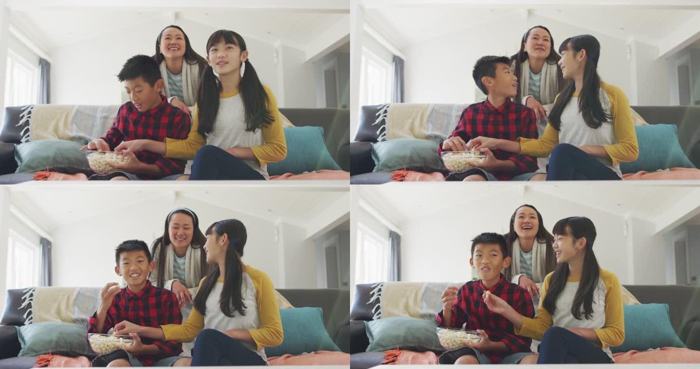 快乐的亚洲母亲在客厅看电视，儿子和女儿坐在沙发上吃爆米花