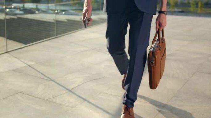 一个穿着棕色鞋子的男人的脚在铺好的街道上行走的视频，前视图