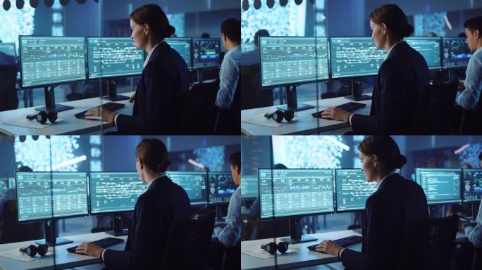 自信的女性数据科学家在神经网络的大型基础设施控制和监控室中的个人计算机上工作。女工程师和同事在办公室