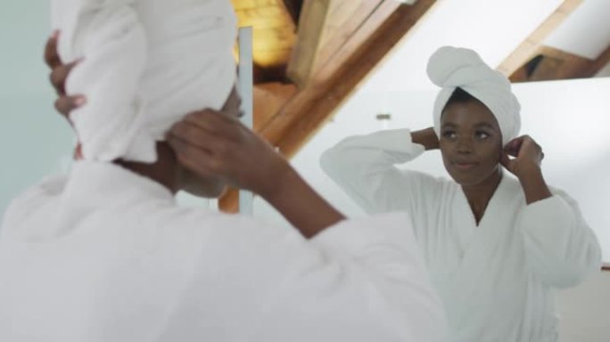 微笑的非裔美国美女把毛巾放在头上，在浴室里看着镜子
