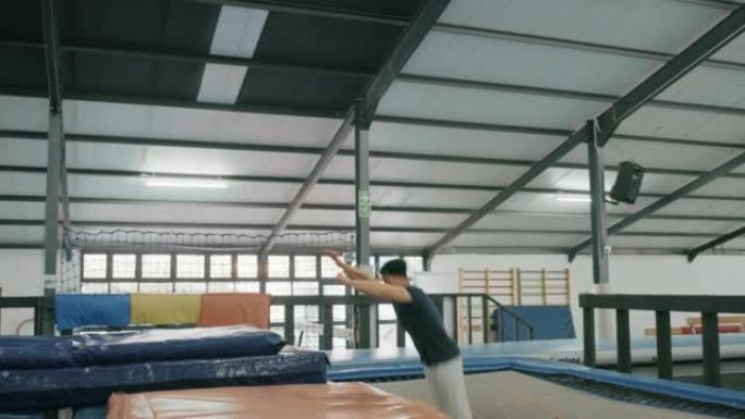体操男子和蹦床空气跳跃与强大的能量翻转特技，用于健身房的健身训练。活跃的运动员男性在体育馆进行健康，