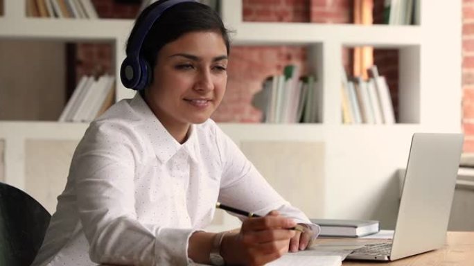年轻的印度妇女戴着耳机听音频课程进行作业