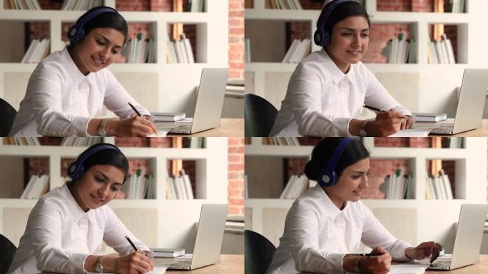 年轻的印度妇女戴着耳机听音频课程进行作业