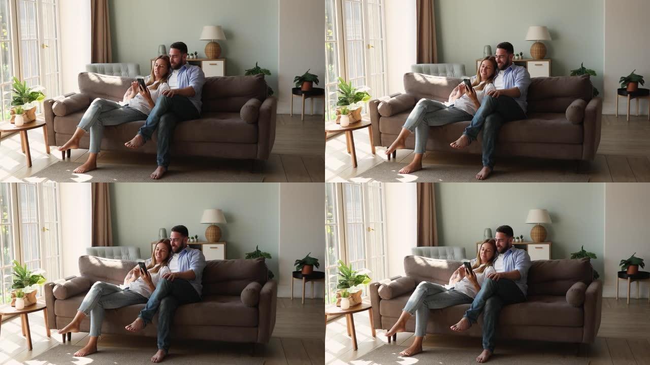 轻松的情侣坐在沙发上使用手机讨论在线购买
