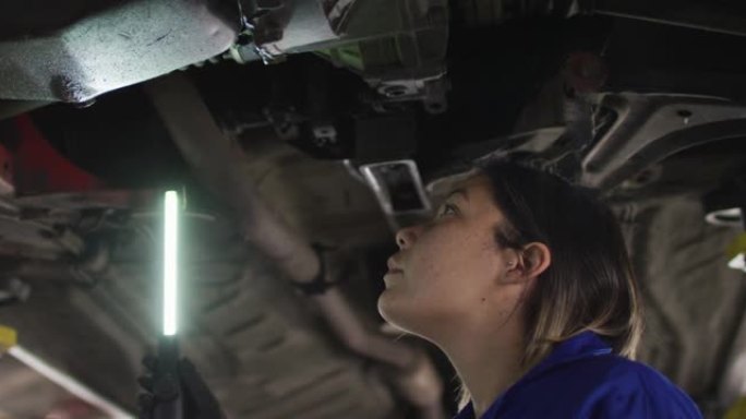 女机械师使用led灯并在汽车服务站的汽车下工作