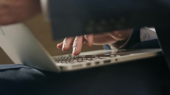 一个男人的手在一个灰色的银色笔记本电脑上打印，该笔记本电脑躺在一个男人的膝盖上，而相机从侧面到正面拍