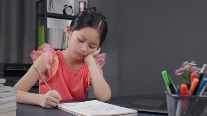 亚洲小女孩在家学习科学和在书上写笔记。家庭学校，电子学习。她在家上学的作业上使用铅笔书写。