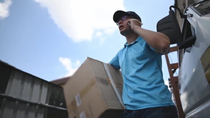 低角度视角亚洲中国成熟男性送货员打电话给客户，在皮卡车旁边拿着纸板箱