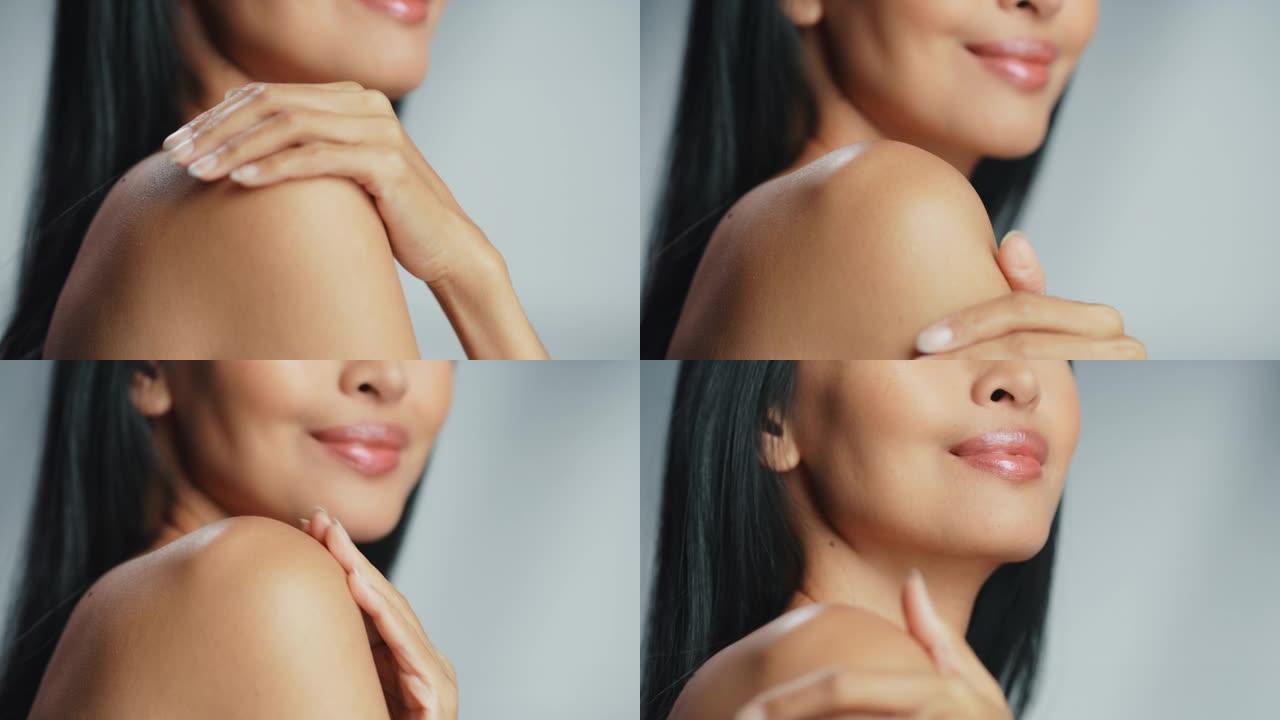 美丽的亚洲女人抚摸着她完美柔软的肩膀，脖子，性感地微笑。享受她美丽的女性。天然化妆品护肤品。孤立背景