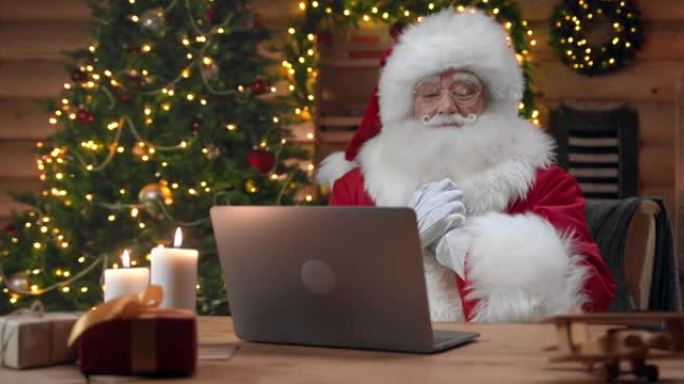 圣诞老人正在使用笔记本电脑进行视频聊天，他喜欢交谈并微笑