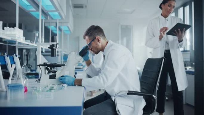 医学发展实验室: 白人男性科学家在显微镜下观察，将数据输入数字平板电脑。高级制药实验室从事医学、生物