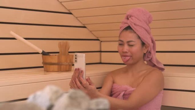 关闭快乐的年轻亚洲女士在芬兰桑拿浴室放松和自拍