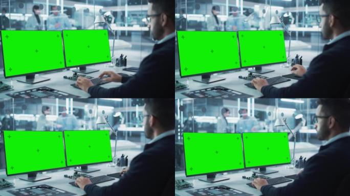 工业工程师在现代技术研发中心的台式计算机上工作，该计算机具有两个绿屏Chromakey显示屏。肩膀上