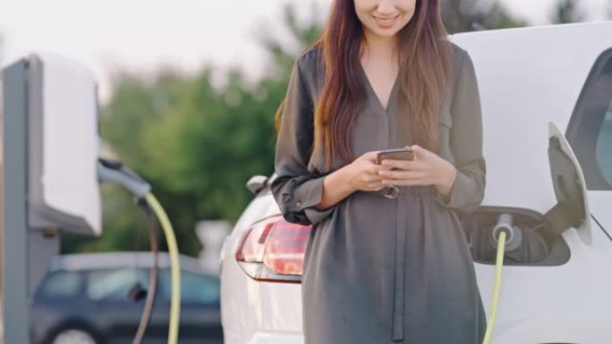 SLO MO女人在充电站等待汽车充电时使用智能手机