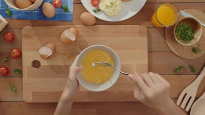 年轻的亚洲女厨师的手将鸡蛋搅拌到陶瓷碗中，用蔬菜在家里厨房桌子上的木板上煮煎蛋。