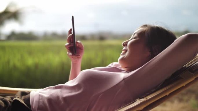 女人在吊床上放松，在阳光明媚的夏天使用智能手机