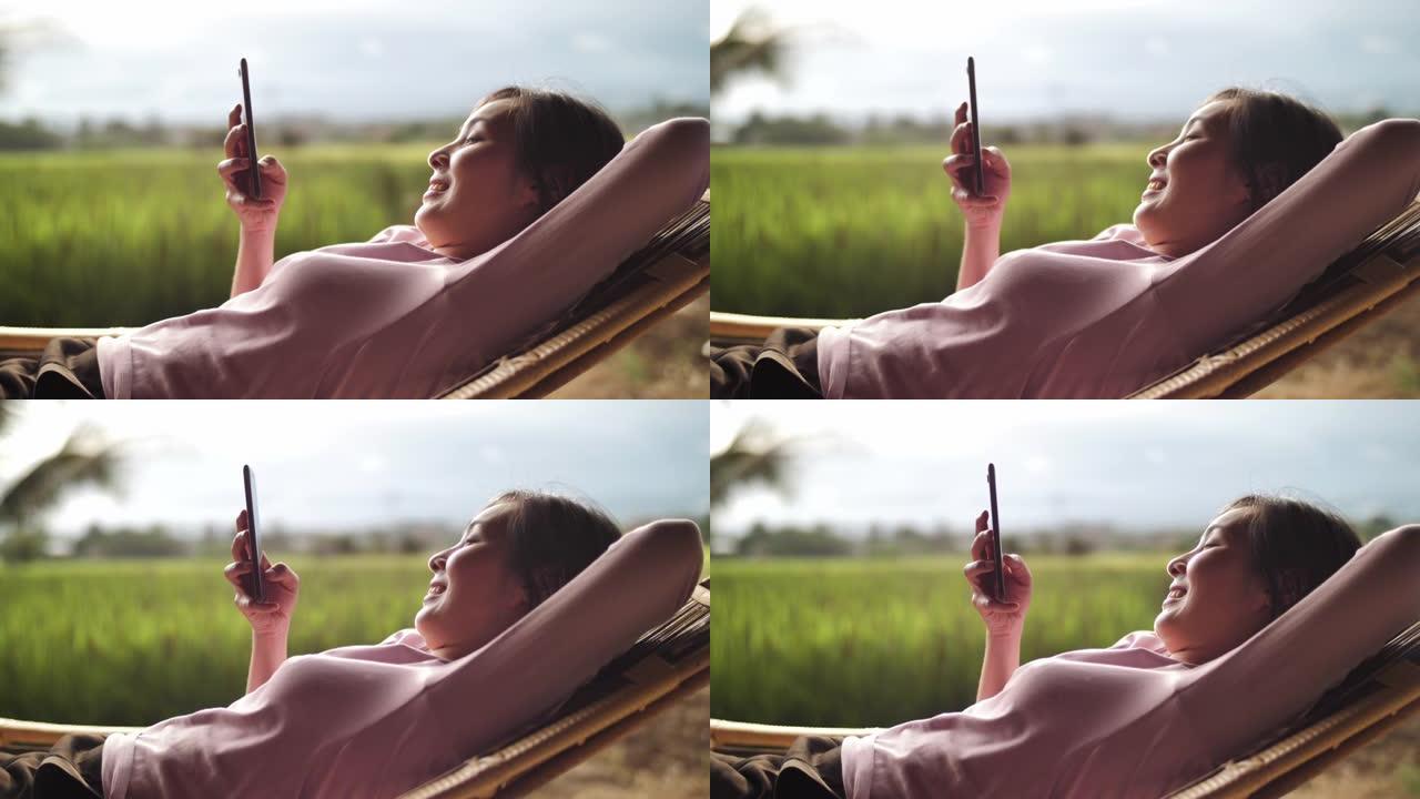 女人在吊床上放松，在阳光明媚的夏天使用智能手机