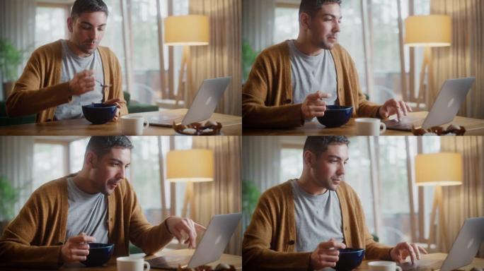 英俊的成年男子使用笔记本电脑，坐在厨房里，在公寓里吃早餐粥或麦片。有魅力的男人正在网上购物，在流媒体