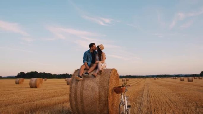 成年夫妇坐在田野上的干草捆上拥抱和亲吻的推入慢动作镜头