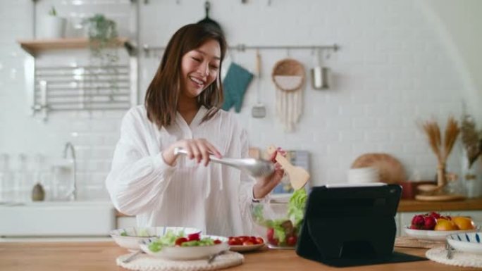 健康女性在数字平板电脑上烹饪沙拉和听音乐