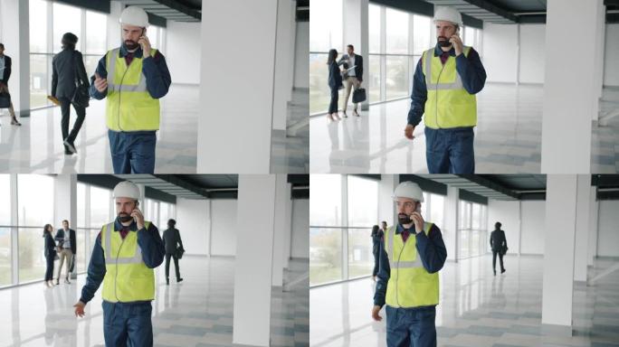 在新楼里，戴着头盔和背心的工程师在手机上讲话的慢动作肖像