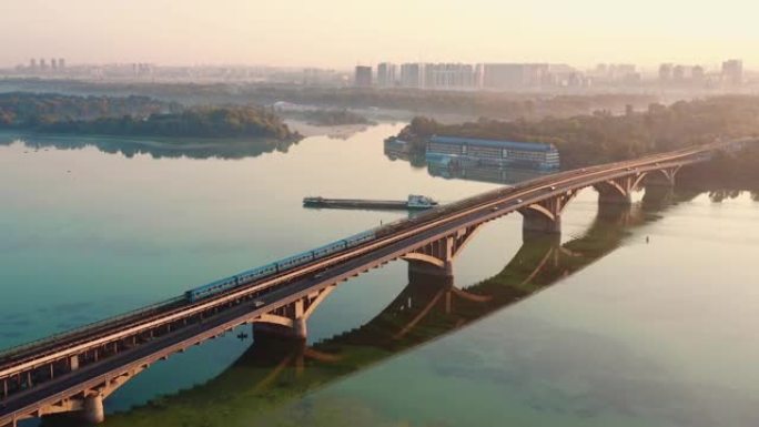 令人惊叹的电影鸟瞰图汽车和火车在令人惊叹的第聂伯河上的桥上以及田园诗般的日出基辅全景。