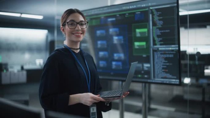 一位戴着眼镜，使用笔记本电脑，看着相机并微笑着的美丽多元化女性的肖像。信息技术专家、软件工程师或开发