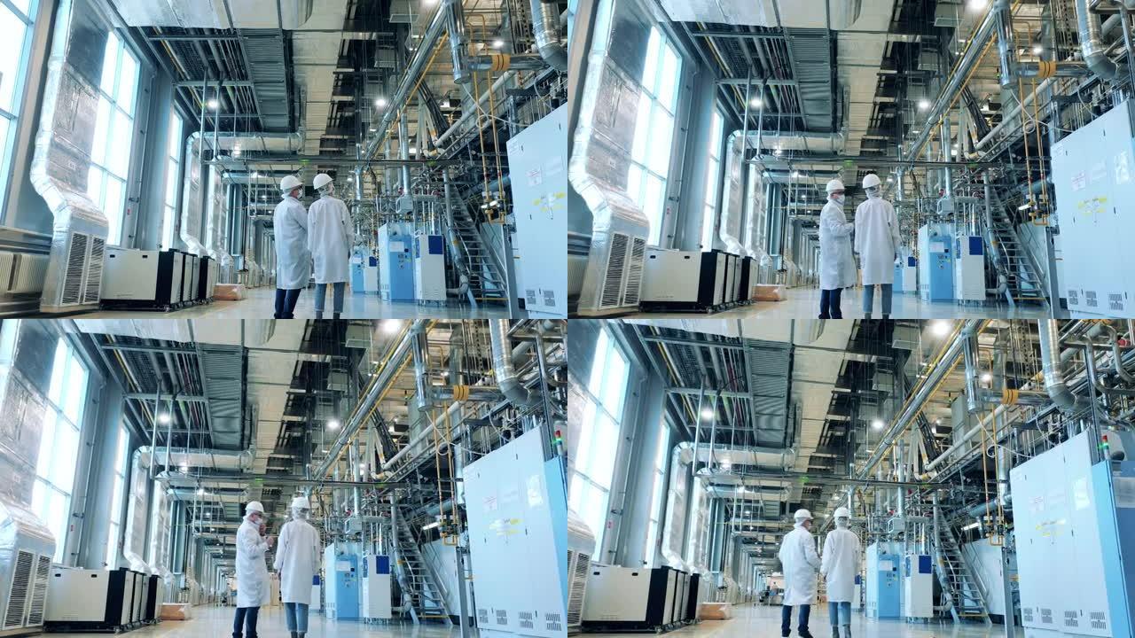 两名身穿实验室外套的专家正在工厂单位穿行。工厂设施，在现代工业工厂工作的工程师。