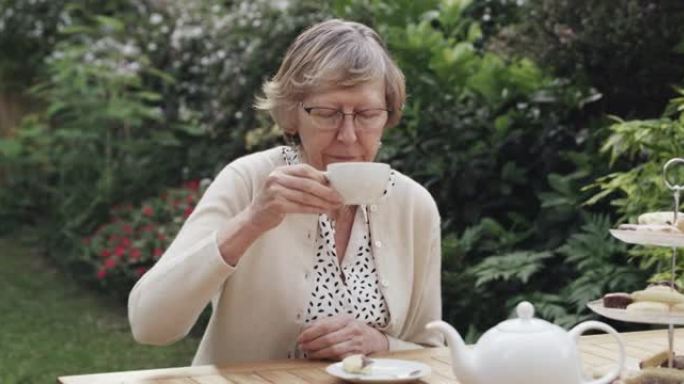 4k视频片段，一名老年妇女在花园里喝杯茶和一些蛋糕