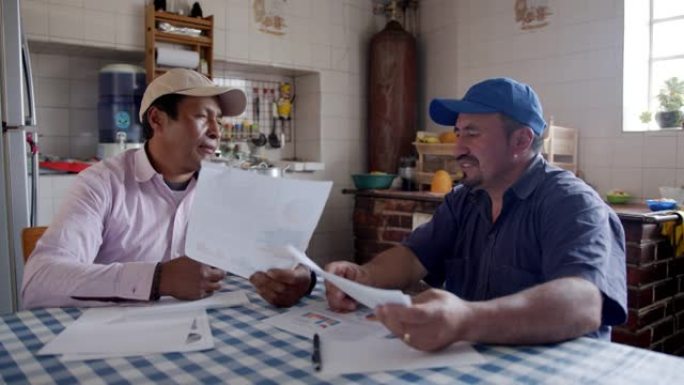 拉丁美洲男性农民在农村家庭中查看文件时讨论业务
