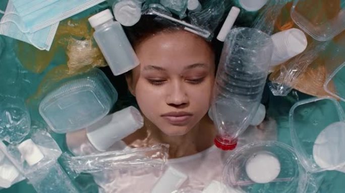 电影的俯视图，年轻混血女子的脸躺在水上，在一次性塑料包装中浪费慢动作。