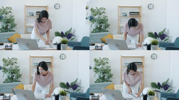 年轻的亚洲女性建筑师与蓝图一起工作，独自在家进行测量