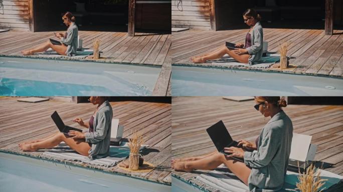 WS年轻女子挂断电话，在游泳池旁的木制露台上打开笔记本电脑
