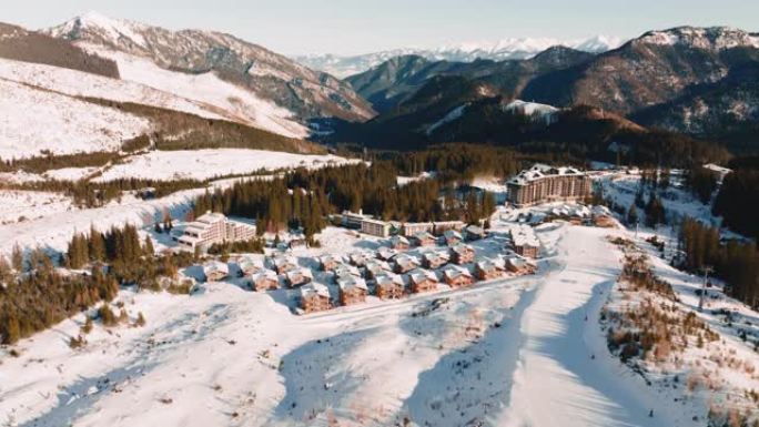 冬季度假胜地的鸟瞰图，带小屋的娱乐中心和阳光明媚的山脉的白雪皑皑的滑雪道斜坡。