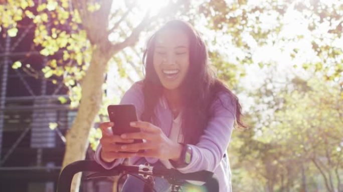 在公园里使用智能手机时，带着自行车微笑的亚洲妇女