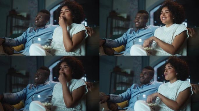 黑人夫妇在电视上看喜剧电影，深夜坐在公寓的沙发上吃爆米花。笑男女朋友在家一起欣赏搞笑电视剧。低角度射