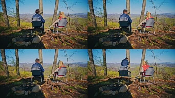 夫妻俩在大自然中露营，既坐在椅子上，又从杯子里喝酒，男人站起来看着风景