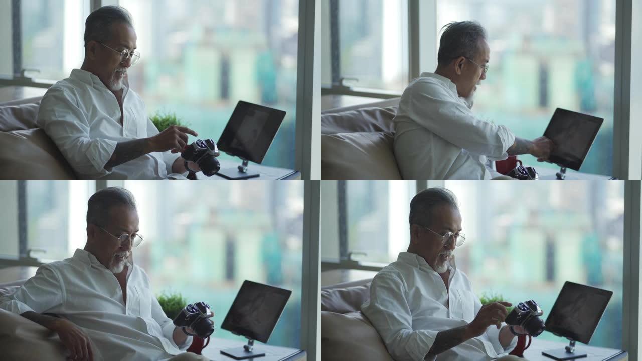 亚洲华人退休老人在客厅放松，看着他的相机和数码平板电脑