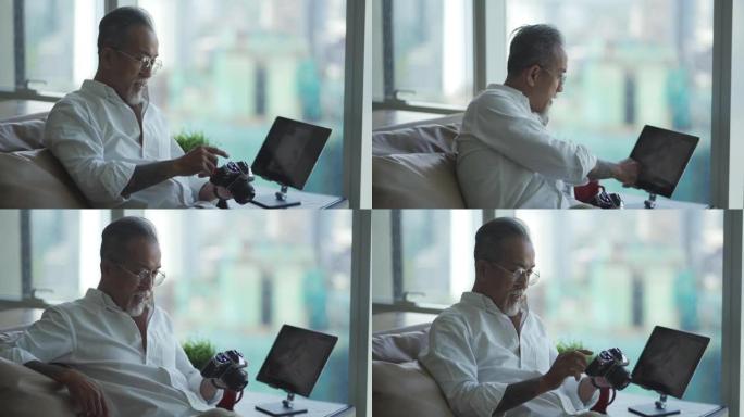 亚洲华人退休老人在客厅放松，看着他的相机和数码平板电脑