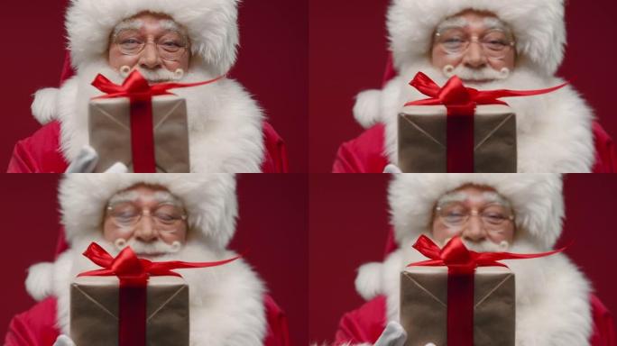 特写镜头一种圣诞老人给我们一个可爱的小礼品盒，带着微笑，站在红色的背景下