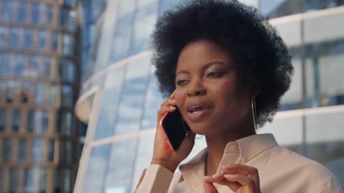 一位肤色黝黑的商务女士礼貌地在电话中讲话，背景为现代玻璃结构