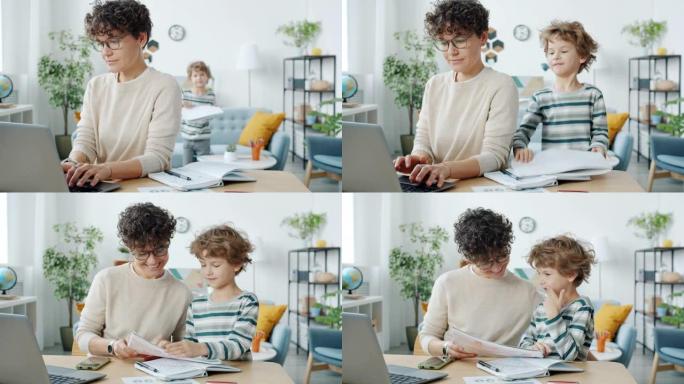工作的母亲使用笔记本电脑，然后拥抱孩子在公寓里一起画画