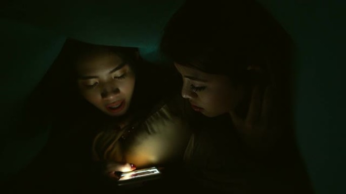 一个年轻女孩或青少年在晚上用手机和某人说话。通过她房间里的屏幕代表了现代技术在日常生活中的使用。