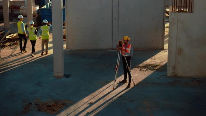 建筑工人使用经纬仪测量光学仪器测量建筑工地上水平和垂直平面的角度。戴着安全帽的工人为建筑物做投影。