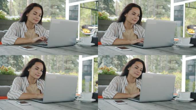 美丽的年轻黑发女人用笔记本电脑打字，享受露天咖啡馆的远程工作